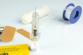 High angle shot of a syringe, bandaids, plastic tape, and pills on a white surface