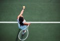 The game begins now. High angle shot of a young woman serving a ball while playing tennis on a court. Royalty Free Stock Photo