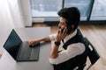 High angle side view of Indian bearded business man in glasses working at laptop sitting at desk and talking on Royalty Free Stock Photo