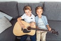 high angle view of adorable little brothers with guitar smiling at camera while sitting on sofa