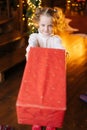 High-angle view of adorable smiling little blonde child girl sending gift box with Christmas present to you looking at Royalty Free Stock Photo