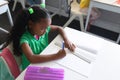 High angle view of african american elementary schoolgirl writing on book at desk classroom Royalty Free Stock Photo