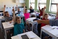 Group of school children sitting at desks and raising their hands to answer Royalty Free Stock Photo