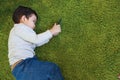 High angle view of asian cute and smart little boy lying on geen floor while using or playing game from cell phone device with Royalty Free Stock Photo