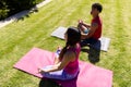 High angle view of biracial young couple meditating while sitting on mats over field in yard Royalty Free Stock Photo