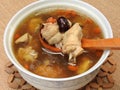 High angle view of a bowl of chicken soup on bamboo mat. It contain Chinese medicine such as goji berry and red jujube.