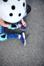 High angle view of boy in safety helmet for skateboard tying shoelaces sitting on asphalt of playground Royalty Free Stock Photo