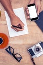 High angle view of businessman hand holding smart phone while writing on notepad Royalty Free Stock Photo