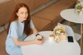 High-angle view of calm happy young woman holding cup of morning hot coffee and thinking sitting at desk in cozy cafe. Royalty Free Stock Photo