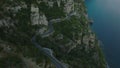 High angle view of cars riving on panoramic route winding on rock cliff high above sea coast. Tilt up revealing