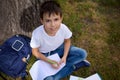 High angle view of a cute boy, elementary aged school child, looking up to camera writing on workbook, doing homework outdoors, Royalty Free Stock Photo