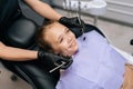 High-angle view of cute little girl smiling looking away sitting in stomatology seat while pediatric dentist in gloves Royalty Free Stock Photo