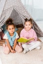 high angle view of cute multiethnic kids sitting on carpet with book and smiling Royalty Free Stock Photo