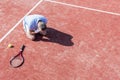 High angle view of disappointed mature man with head in hands while kneeling by tennis racket on red court during summer Royalty Free Stock Photo