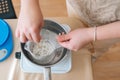 High-angle view of female artisan mixing ingredients for hand candle-making in glass jar into pot of boiling water for