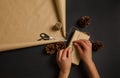 High angle view of female hands wrapping Christmas present in craft paper tying bow with rope on black surface with brown Royalty Free Stock Photo