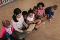 Female teacher teaching schoolkids and sitting on floor of school library Royalty Free Stock Photo