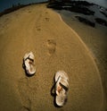 High-angle view of flip-flops and feet track on the sand