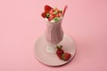 High angle view of glass of milkshake with drinking straw, candies and strawberries on plate