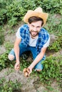 high angle view of handsome farmer squatting in field at farm and holding