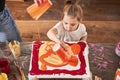 Child blonde girl pouring fresh orange paints into the canvas while creating her own masterpiece Royalty Free Stock Photo