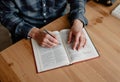Close up of a Person s Hands Writing Notes in an Open Book on a Wooden Desk Royalty Free Stock Photo