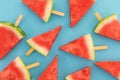 High angle view of multiple watermelon triangles on wooden sticks on blue background