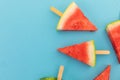 High angle view of multiple watermelon triangles on wooden sticks on blue background