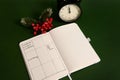 Top view of an opened page of notepad with plans for day, alarm clock and snowy branch of holly Christmas plant isolated on green