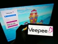 High angle view of person holding cellphone with logo of French retail platform Veepee on screen in front of website.