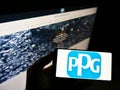 High angle view of person holding cellphone with logo of US chemicals company PPG Industries Inc on screen with web page.