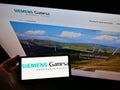 High angle view of person holding smartphone with logo of engineering company Siemens Gamesa Renewable Energy S.A. on display.