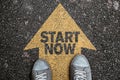 High angle view of person standing on arrow marking on asphalt, road with text START NOW