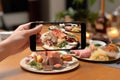 High angle view of person& x27;s hand with smartphone photographing appetizing dish in eatery