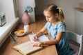High-angle view of pretty elementary child school girl writing to notebook with pen looking on paper book. Royalty Free Stock Photo