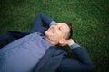 Happy Young businessman in a suit lying on the green grass and relaxing in park. Royalty Free Stock Photo