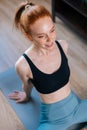 High-angle view of smiling redhead young woman wearing sportswear sitting in floor on yoga mat. Royalty Free Stock Photo