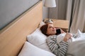 High-angle view of smiling young woman lying on cosy bed at home and talking mobile phone after waking up in morning at Royalty Free Stock Photo