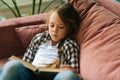 High-angle view of tired adorable child kid girl reading paper book lying on soft couch at home looking at camera. Royalty Free Stock Photo