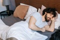 High-angle view of tired bearded young man sleeping peacefully lying on side in large comfortable double bed under white Royalty Free Stock Photo