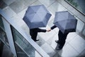 High angle view of two businessmen holding umbrellas and shaking hands in the rain