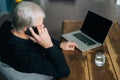 High-angle view of unrecognizable gray-haired senior adult man talking on mobile phone sitting at desk with laptop Royalty Free Stock Photo