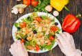 High angle view of unrecognizable hands in gloves lays out tomatoes in salad with mix of lettuce leaves, shrimps, olives and Royalty Free Stock Photo