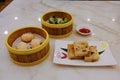 High angle view of a variety of traditional dim sum dishes on dining table in restaurant. Dumplings in bamboo steamer baskets, and