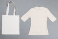 High angle view of white canvas bag and white t shirt with copy space on grey background Royalty Free Stock Photo