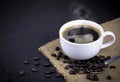 High angle view of white ceramic cup of black hot Americano coffee with steam on a sackcloth with a pile of roasted coffee beans Royalty Free Stock Photo