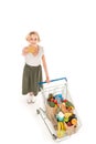 high angle view of young woman holding credit card and smiling at camera while standing with shopping trolley full of grocery Royalty Free Stock Photo