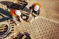 High angle of workers in white helmets arranging paving stones