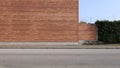 High brick wall facade with brick fence and a hedge on the right. Sidewalk and street in front Royalty Free Stock Photo