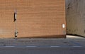 High brick wall, with sidewalk, street signs and asphalt road in front. Narrow alley on the right.